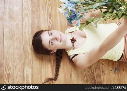 High angle view of a young woman lying on the floor and holding up a bunch of flowers