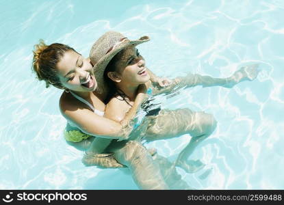 High angle view of a young woman riding piggyback on a young woman in a swimming pool