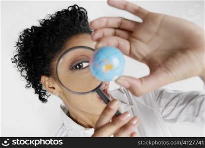 High angle view of a young woman scrutinizing a globe with a magnifying glass