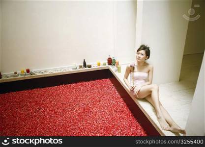 High angle view of a young woman sitting near a hot tub and holding a flower