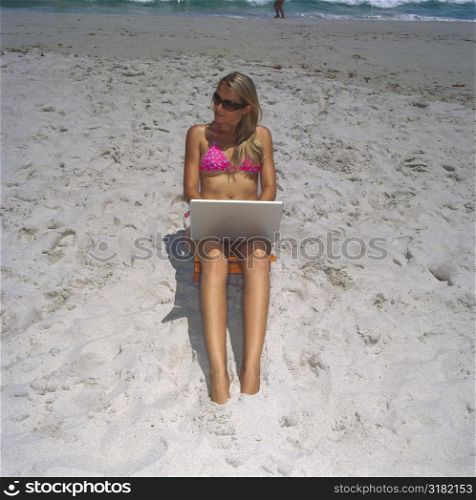High angle view of a young woman sitting on the beach with a laptop
