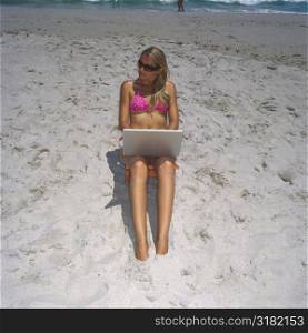 High angle view of a young woman sitting on the beach with a laptop