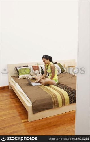 High angle view of a young woman sitting on the bed and using a laptop