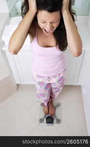 High angle view of a young woman standing on a weighing scale with her hands in hair