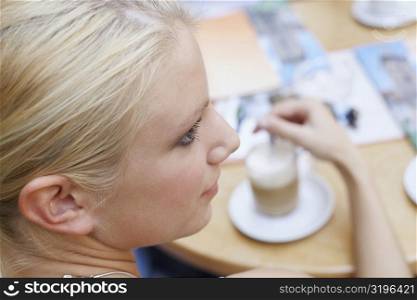 High angle view of a young woman stirring coffee