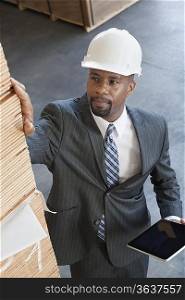 High angle view of African American male contractor inspecting wooden planks while holding tablet PC