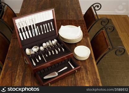 High angle view of an open cutlery box with stacks of plates on a dining table