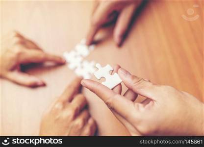 High Angle View Of Businesspeople Hand Solving Jigsaw Puzzle On Wooden Desk