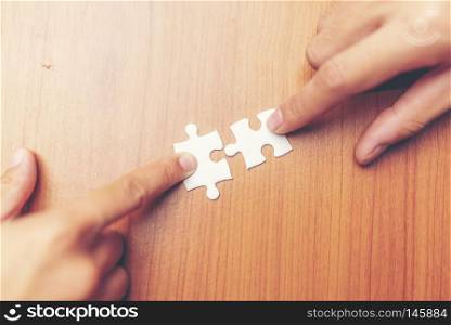 High Angle View Of Businesspeople Hand Solving Jigsaw Puzzle On Wooden Desk