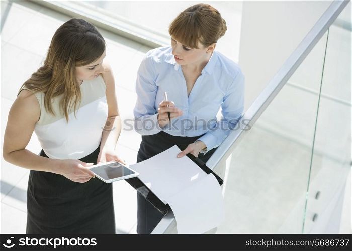High angle view of businesswomen discussing over tablet PC and documents by railing in office