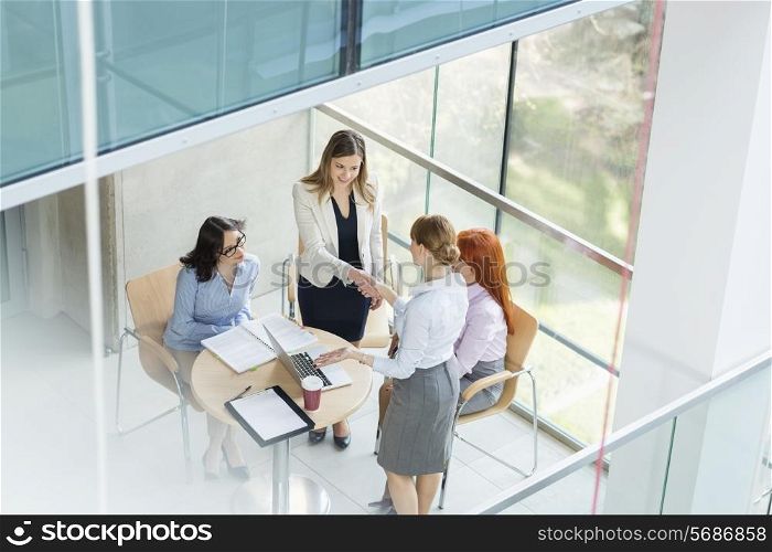 High angle view of businesswomen shaking hands at table in office