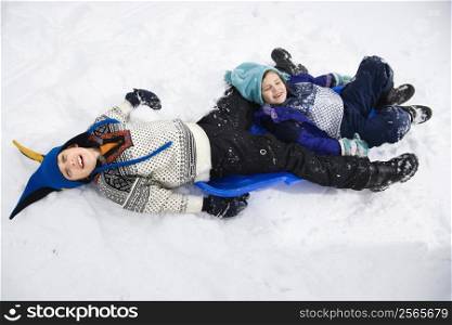 High angle view of Caucasian boy and girl lying on sled in snow.