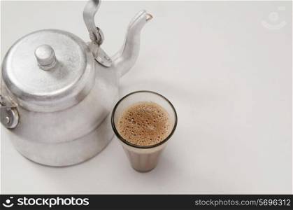 High angle view of chai in glass with an old fashioned kettle isolated over white background