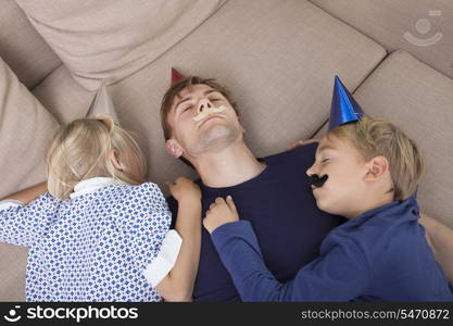 High angle view of children and father with artificial mustache and party hat sleeping on sofa bed