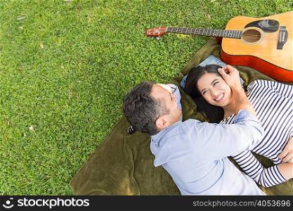 High angle view of couple lying on grass with acoustic guitar smiling