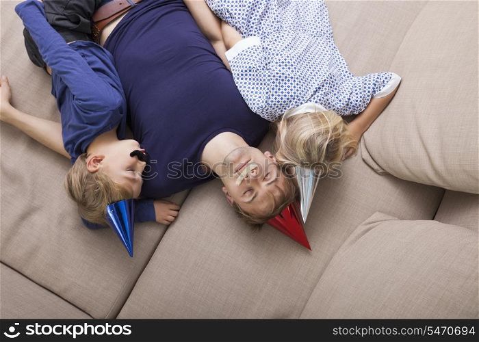 High angle view of father and children with artificial mustache and party hat sleeping on sofa bed