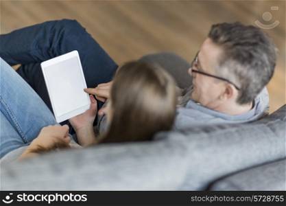 High angle view of father and daughter using digital tablet on sofa