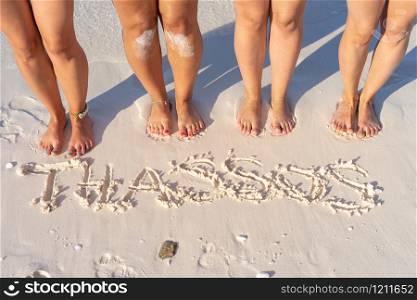 High angle view of four female legs barefoot feet standing on the sand beach by the Thassos written on the sand