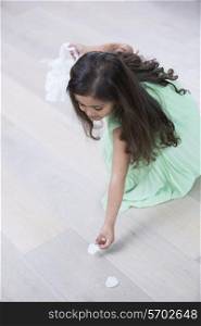 High angle view of girl picking up flower petals from floor at home