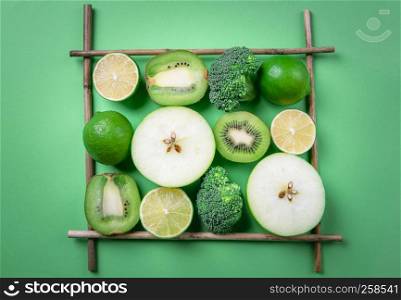 High angle view of green fruits and vegetables displayed in a square frame from wood sticks. Dieting food. Detox context. Vegetarian lifestyle.