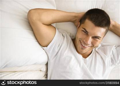 High angle view of handsome Caucasian mid adult man lying with hands behind head smiling.