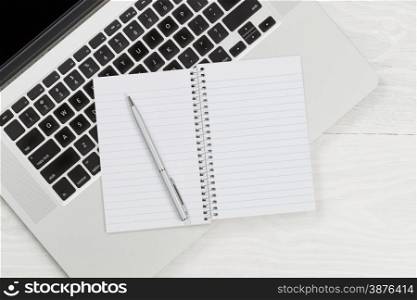 High angle view of laptop and blank notepad with silver pen on rustic white desktop.