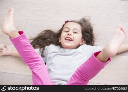 High angle view of playful girl lying on floor with legs raised at home