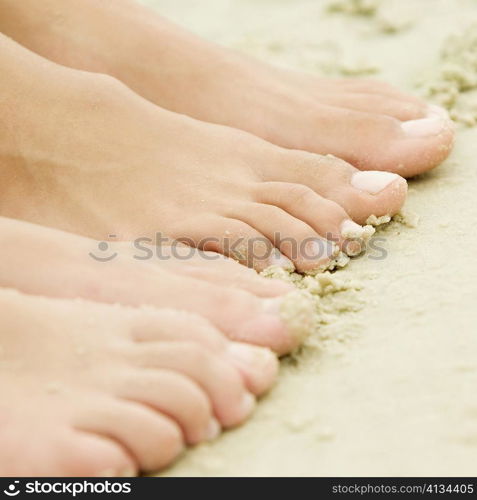 High angle view of the feet of two people on sand