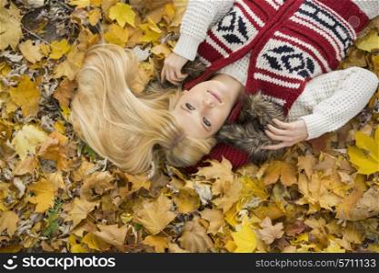 High angle view of thoughtful young woman lying on autumn leaves in park