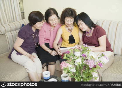 High angle view of three senior women and a mature woman sitting on a couch and looking at a photo album