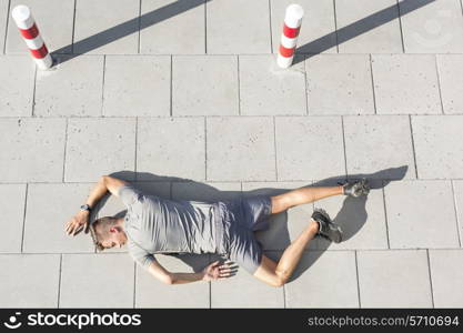 High angle view of tired sporty man lying on sidewalk