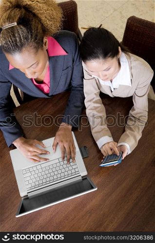 High angle view of two businesswomen using a laptop and a calculator