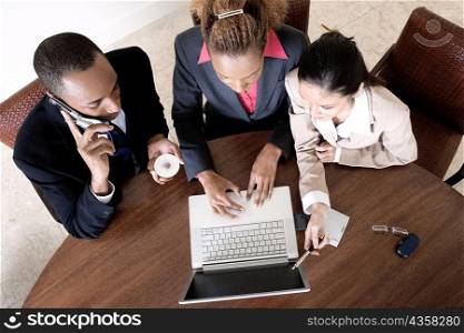 High angle view of two businesswomen using a laptop with a businessman talking on a mobile phone