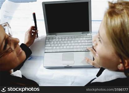 High angle view of two businesswomen working on a laptop and smiling