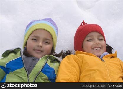 High angle view of two girls lying in snow and smiling