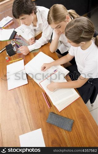 High angle view of two schoolgirls and a schoolboy studying in a classroom