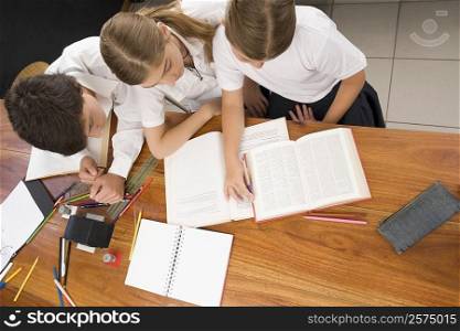 High angle view of two schoolgirls and a schoolboy studying together in a classroom