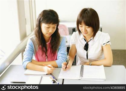 High angle view of two young women holding pens and looking at a spiral notepad