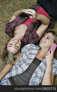 High angle view of two young women lying in a park and using mobile phones