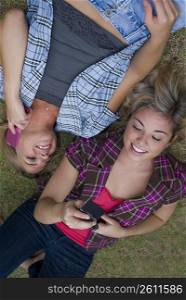 High angle view of two young women lying in a park and using mobile phones