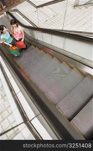 High angle view of two young women standing on an escalator with shopping bags