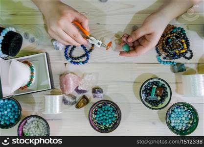 High angle view of Young woman making crystal jewelery necklace and bracelet at home manually