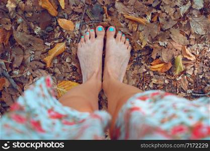 High angle view on naked feet of woman standing barefoot on the dry leaves in the woods nature park in autumn day unshod barefooted