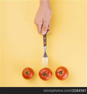 high angle view person s hand inserting fork red tomato yellow background