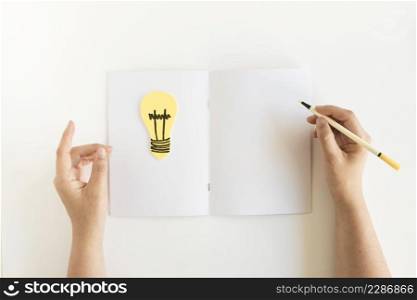 high angle view person s hand writing card with light bulb