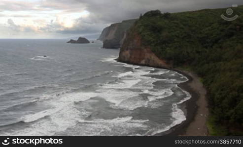 High angle view point of Polulu Valley in Hawaii where giant cliffs meet drop off into the ocean next to a rare black sand beach