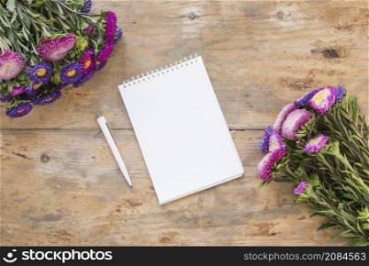 high angle view spiral notepad pen bouquet flowers wooden desk