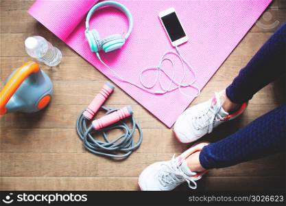 High angle view sporty woman&rsquo;s legs with sport shoes and fitness. High angle view sporty woman&rsquo;s legs with sport shoes and fitness equipments, Mobile phone and headphones on yoga mat, Healthy concept