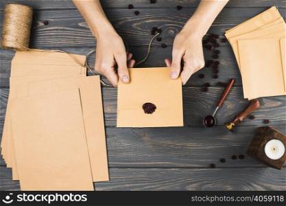 high angle view woman showing seal brown envelop with craft material wooden table