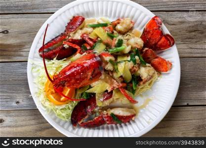 High angled view freshly cooked whole Maine lobster covered with herbs, onions, and sauce on white plate.